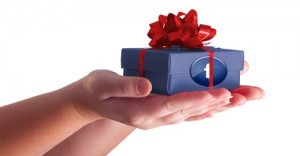 A hand holding a small blue gift box wrapped with a red ribbon and Facebook's logo on the side.